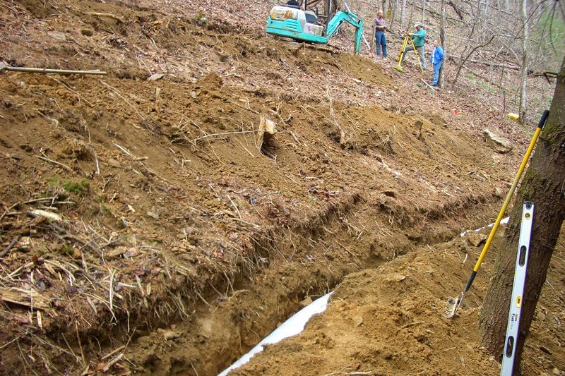 Narrow drain-field trench cut across a steep slope